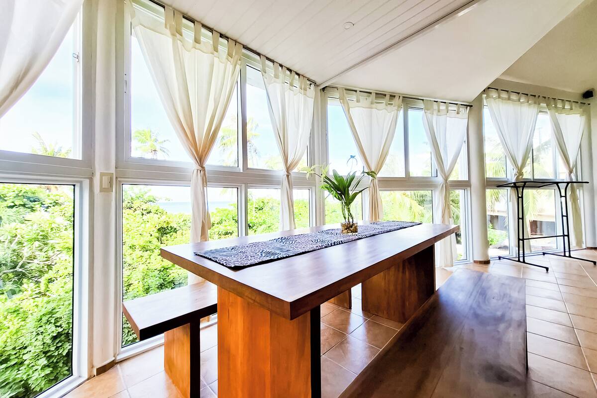 A spacious room with large windows, a wooden table, and a potted plant.