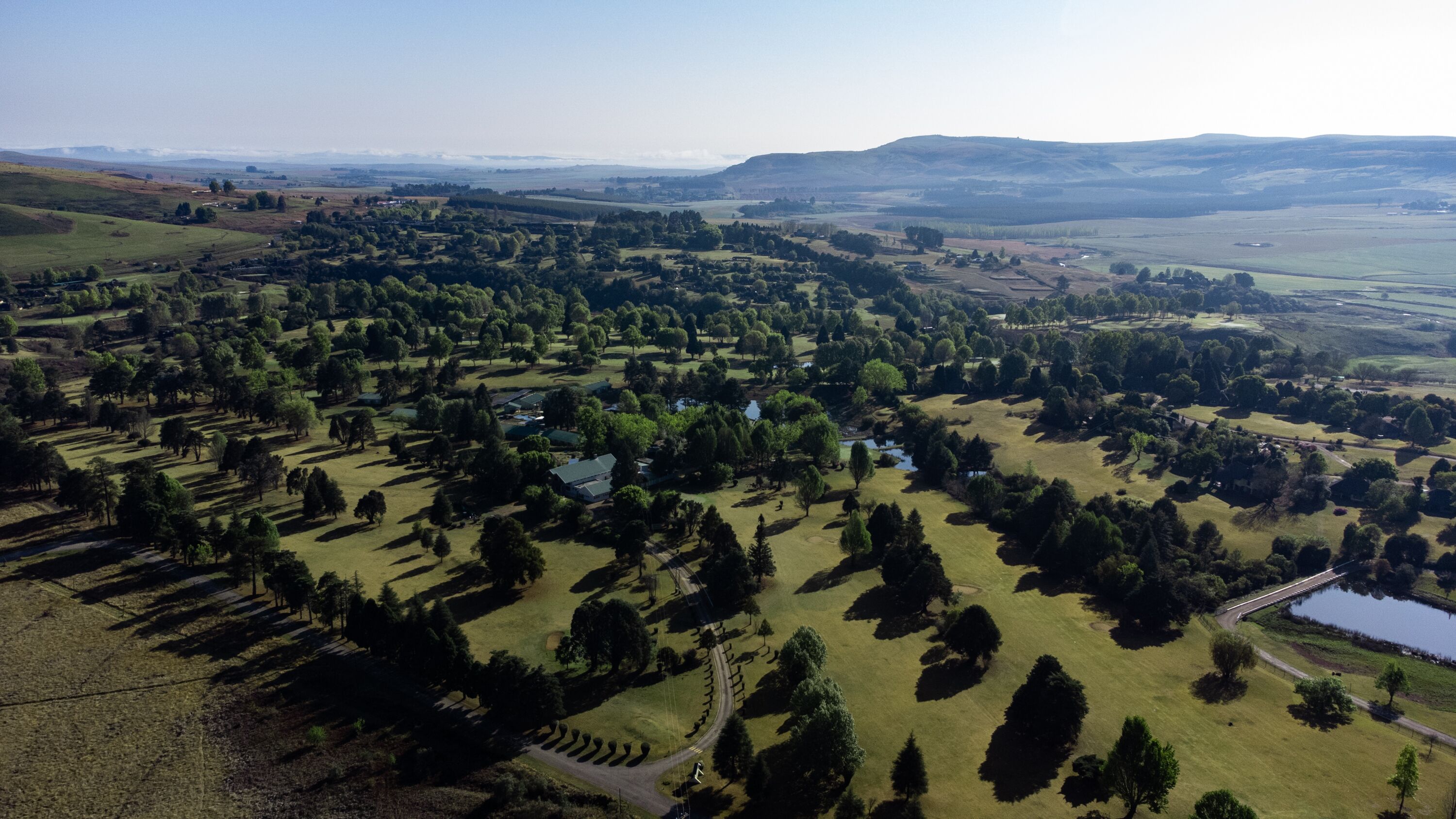 An aerial view of a rural landscape with fields, trees, and a small body of water.