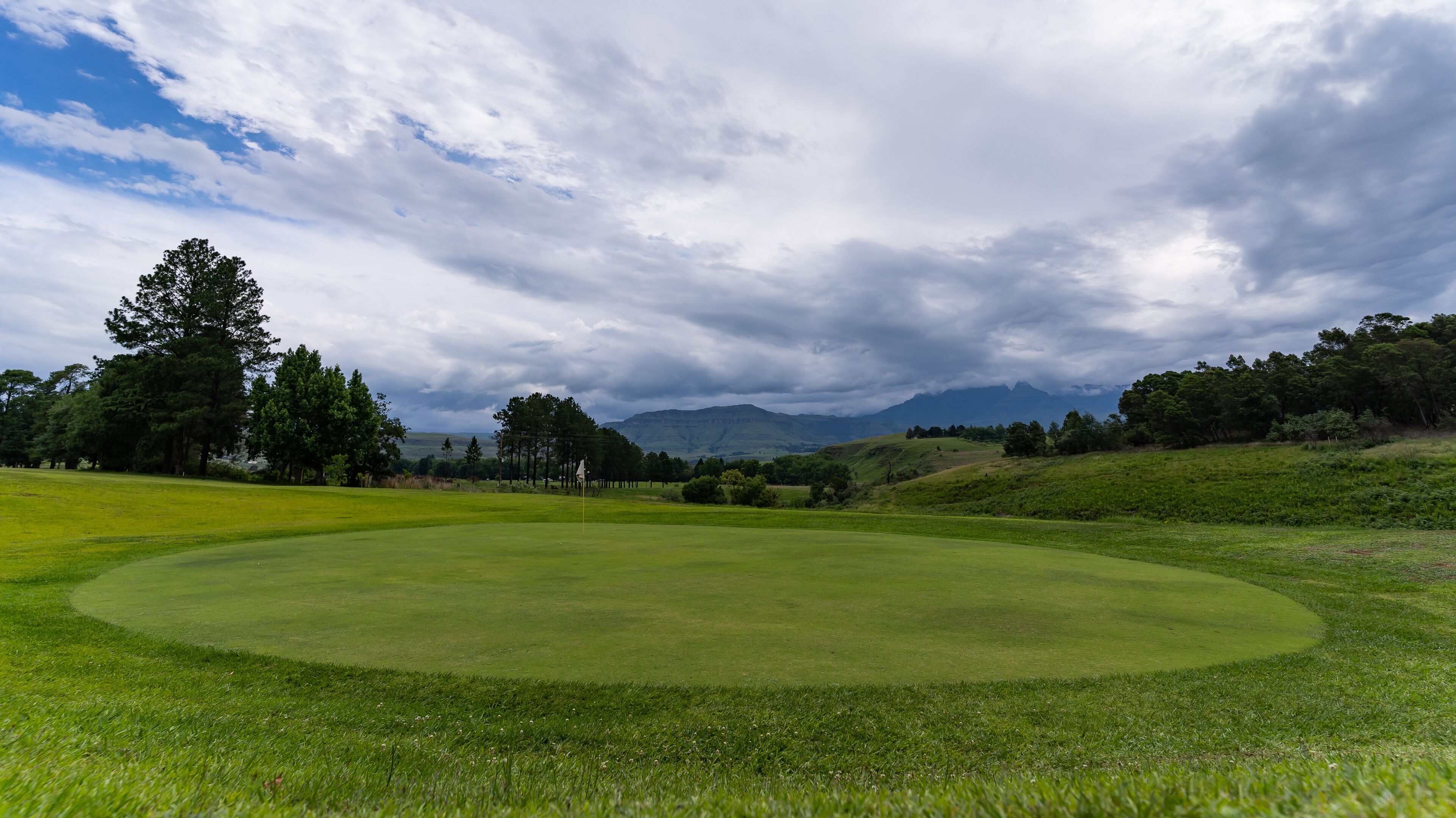 Un parcours de golf doté d’un gazon bien entretenu, d’arbres et d’un paysage montagneux en arrière-plan.