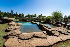 A swimming pool with natural rock formations and a covered area with a roof. - Gooderson Monks Cowl Golf Resort (Cathkin Park)