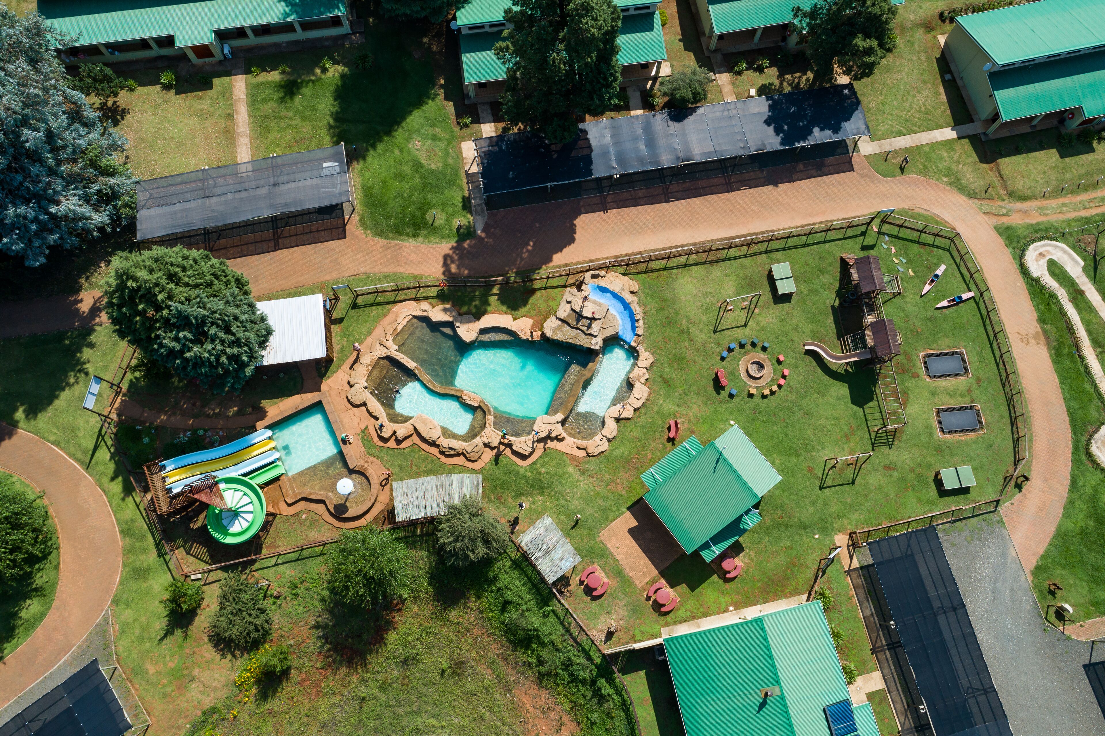 Luchtbeeld van een resort met een zwembad, waterglijbanen en een omheind terras met ligbedden.