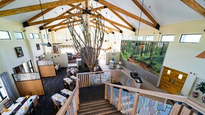 Een ruime hotel lobby met een hoge plafond, houten balken, een trap met leuning en een eetgedeelte met gedekte tafels voor gasten.