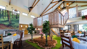 Een restaurant met een eetgedeelte met tafels, stoelen en een centrale tuin met kunstplanten en bomen.