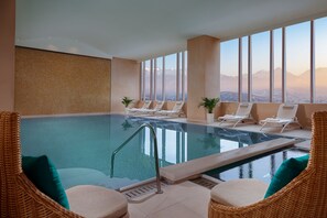 An indoor swimming pool with lounge chairs and a view of mountains.