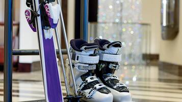 A pair of skis and ski boots leaning against a metal pole in a well-lit indoor area with a reflective floor and decorative lights in the background.