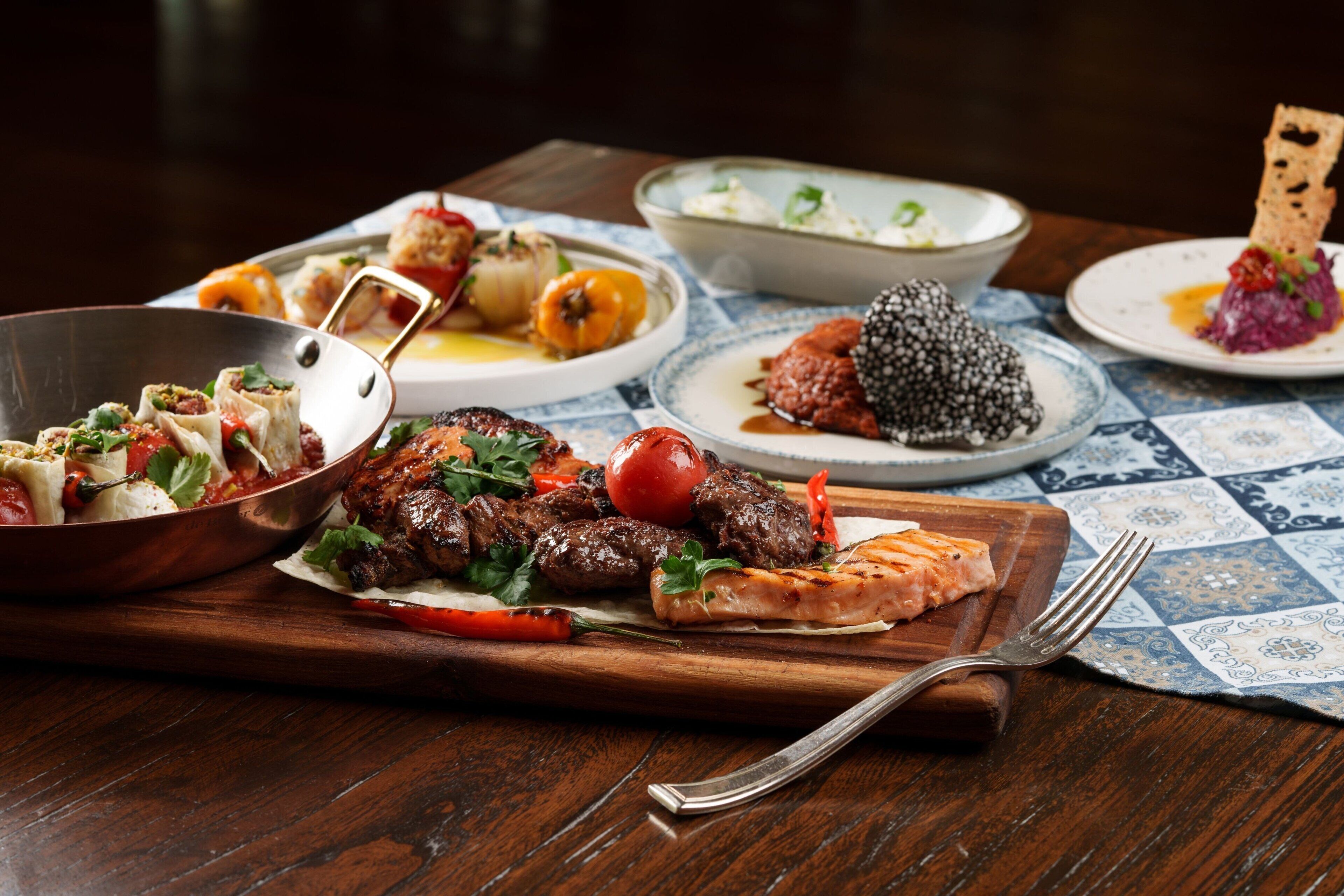 Una mesa de madera con diversos platos, incluyendo carne a la parrilla, verduras y un tazón de sopa.