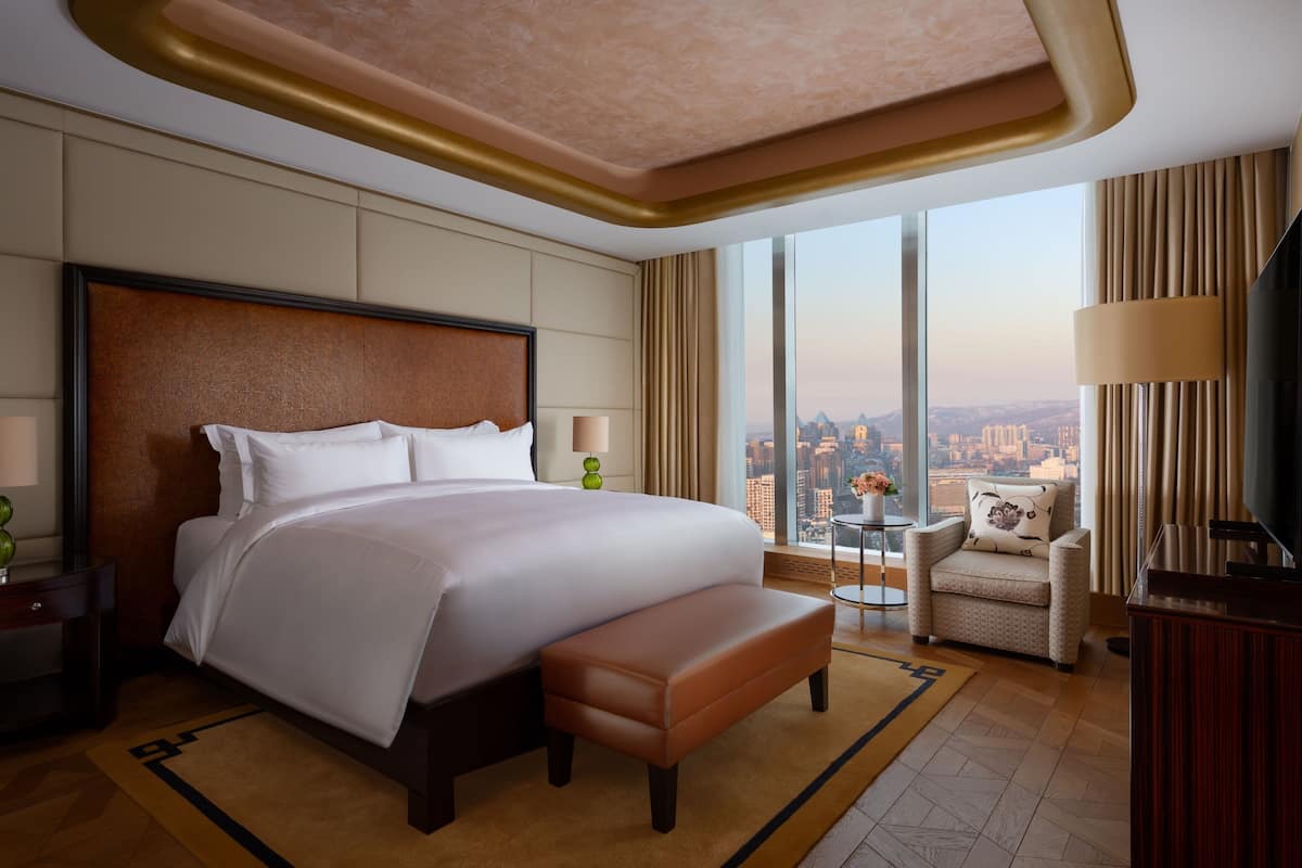 A spacious hotel room with a large bed, a seating area, and a view of the city.