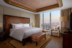 A spacious hotel room with a large bed, a seating area, and a view of the city.