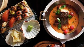 Variedad de platos, incluyendo sushi, un pescado en salsa cremosa y carne a la parrilla.
