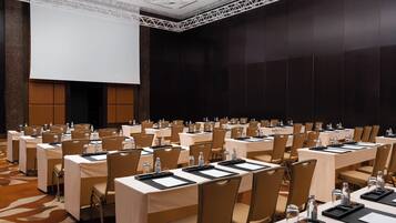 A conference room with rows of tables, chairs, and a large screen.