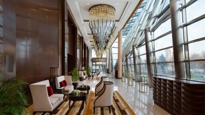 A spacious lobby with a modern chandelier, comfortable seating, and large windows offering a view of the city. - The Ritz-Carlton, Almaty (Almaty)