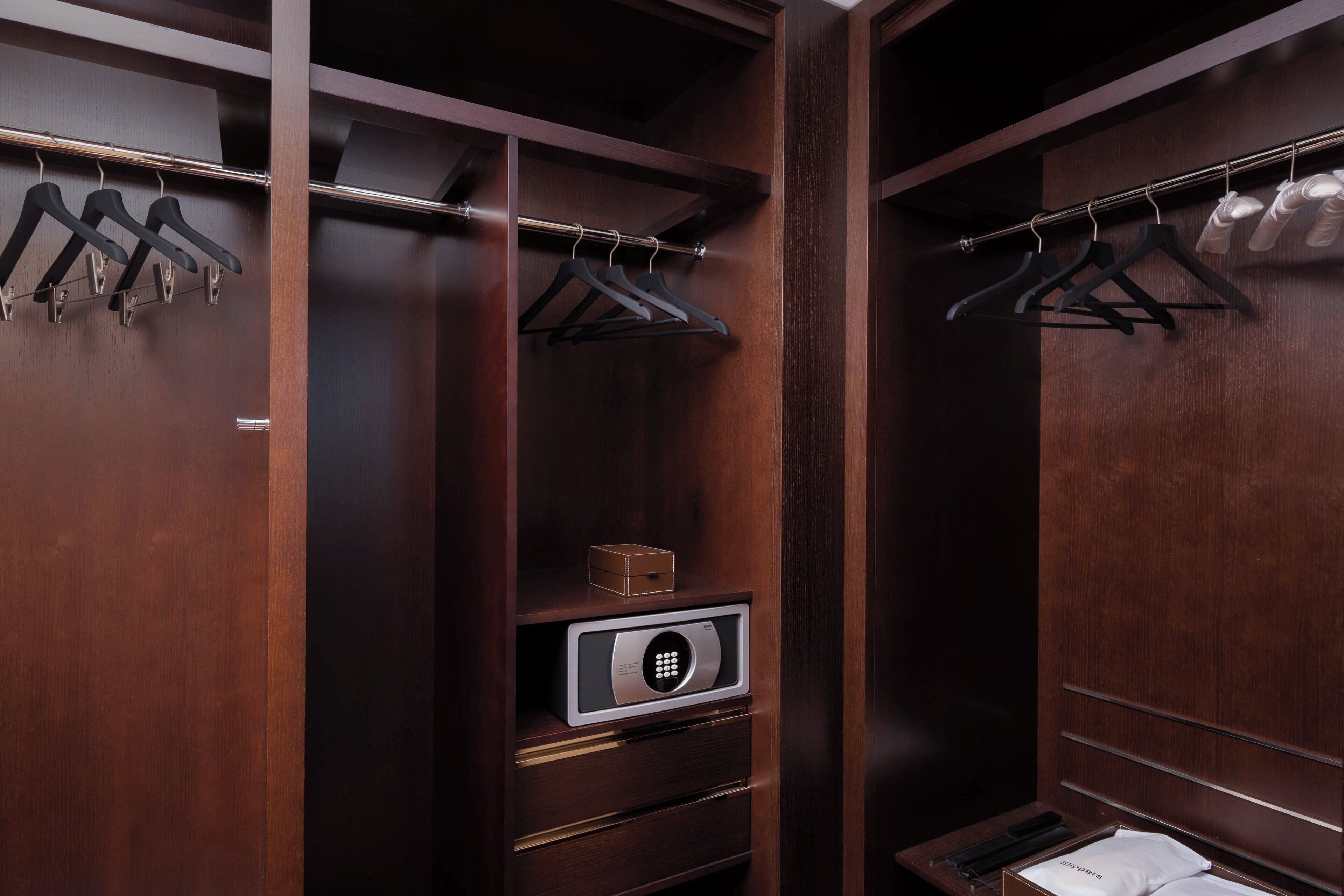 Un vestidor con puertas de madera, múltiples percheros, un zapatero, una caja fuerte y un pequeño contenedor de almacenamiento.