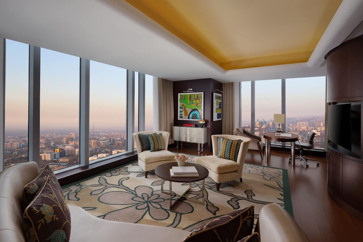 A high-rise apartment with a city view, two sofas, a coffee table, a TV, and a small desk.