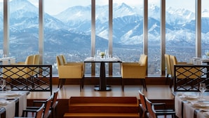 A dining area with a mountain view, featuring tables set with white tablecloths and chairs. - The Ritz-Carlton, Almaty (Almaty)