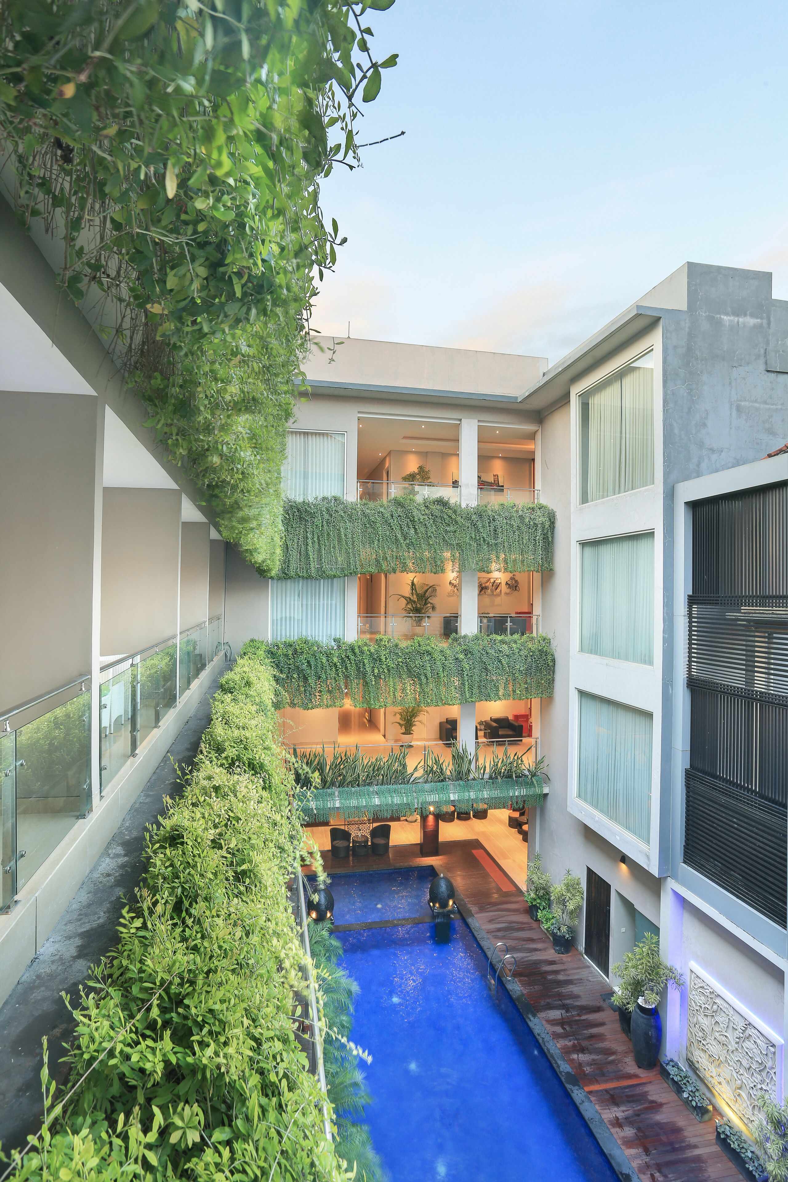 Un edificio moderno con un patio central, una piscina y varios balcones con vegetación.