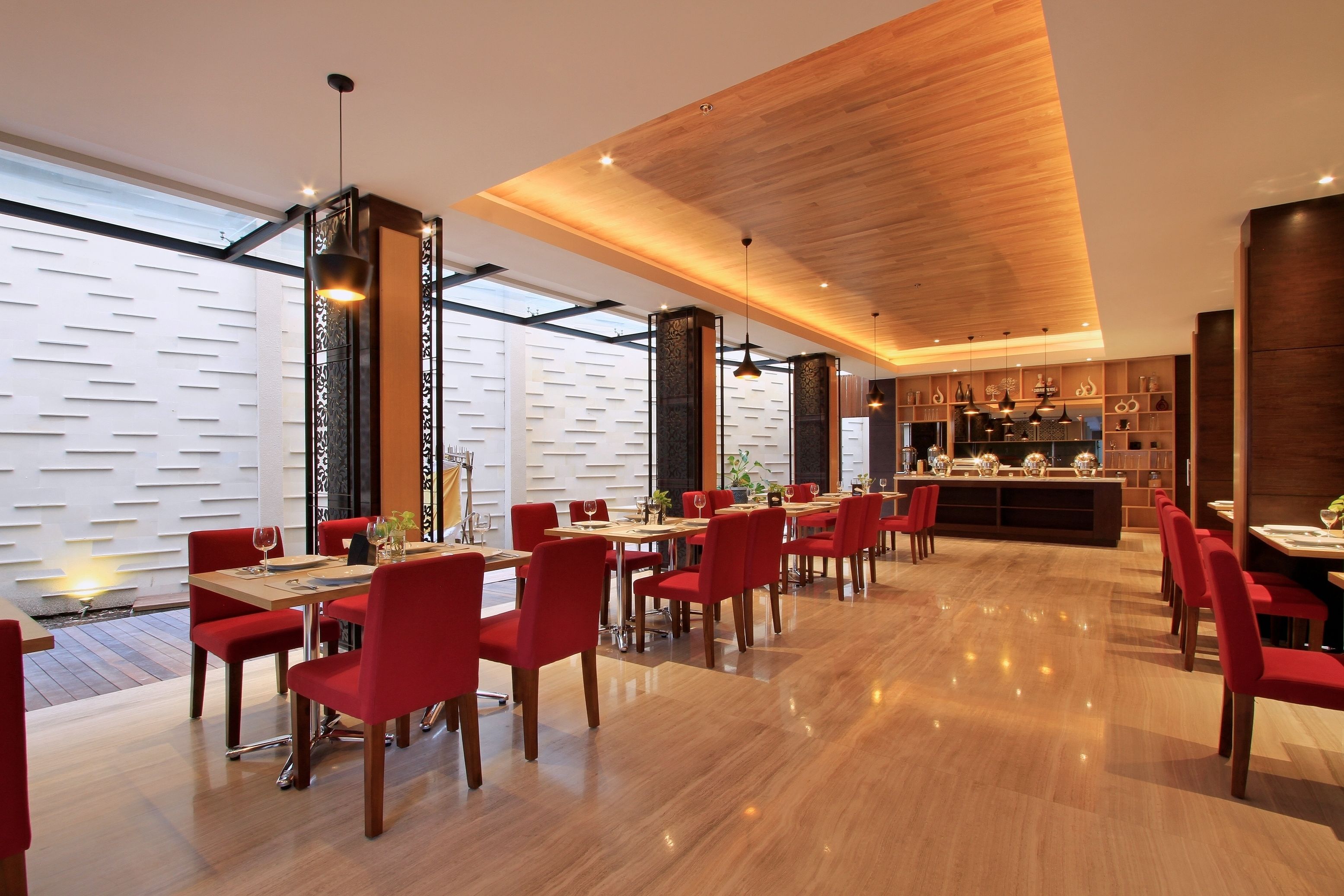 A modern dining area with wooden flooring, red chairs, and a central bar area.