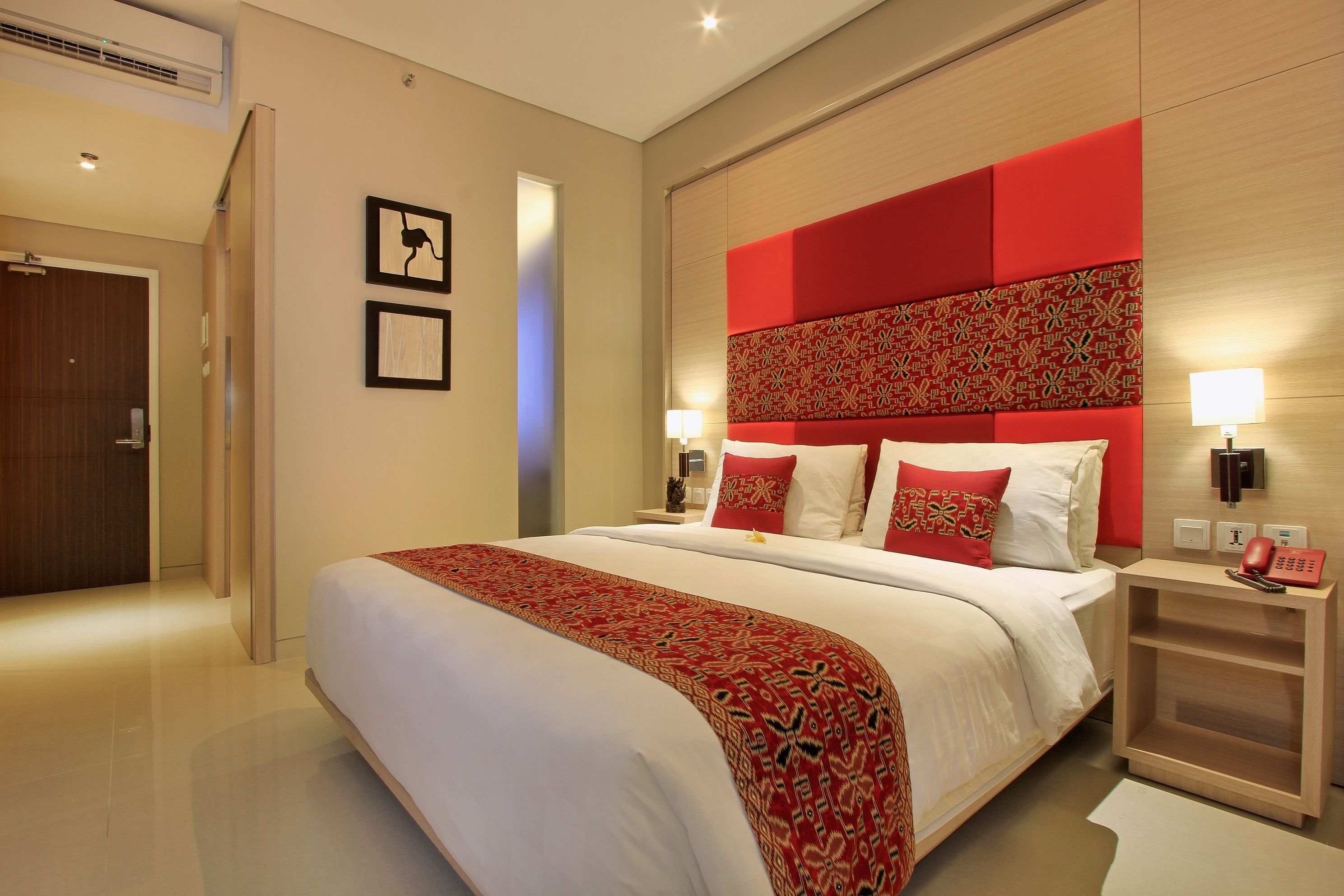 Une chambre d’hôtel moderne avec un grand lit, un mur d’accent rouge et une table de chevet dotée d’une lampe et d’un téléphone.