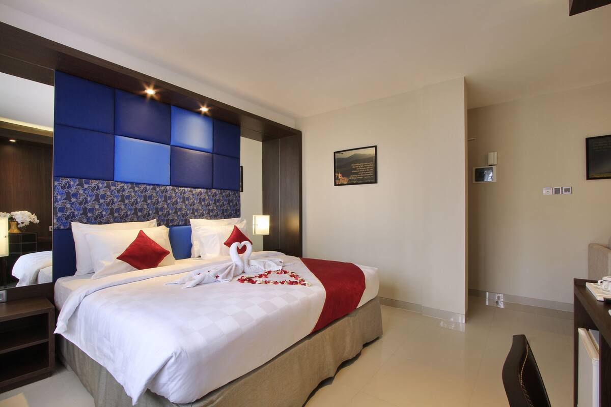 A hotel room with a large bed, a blue headboard, and a red throw blanket.