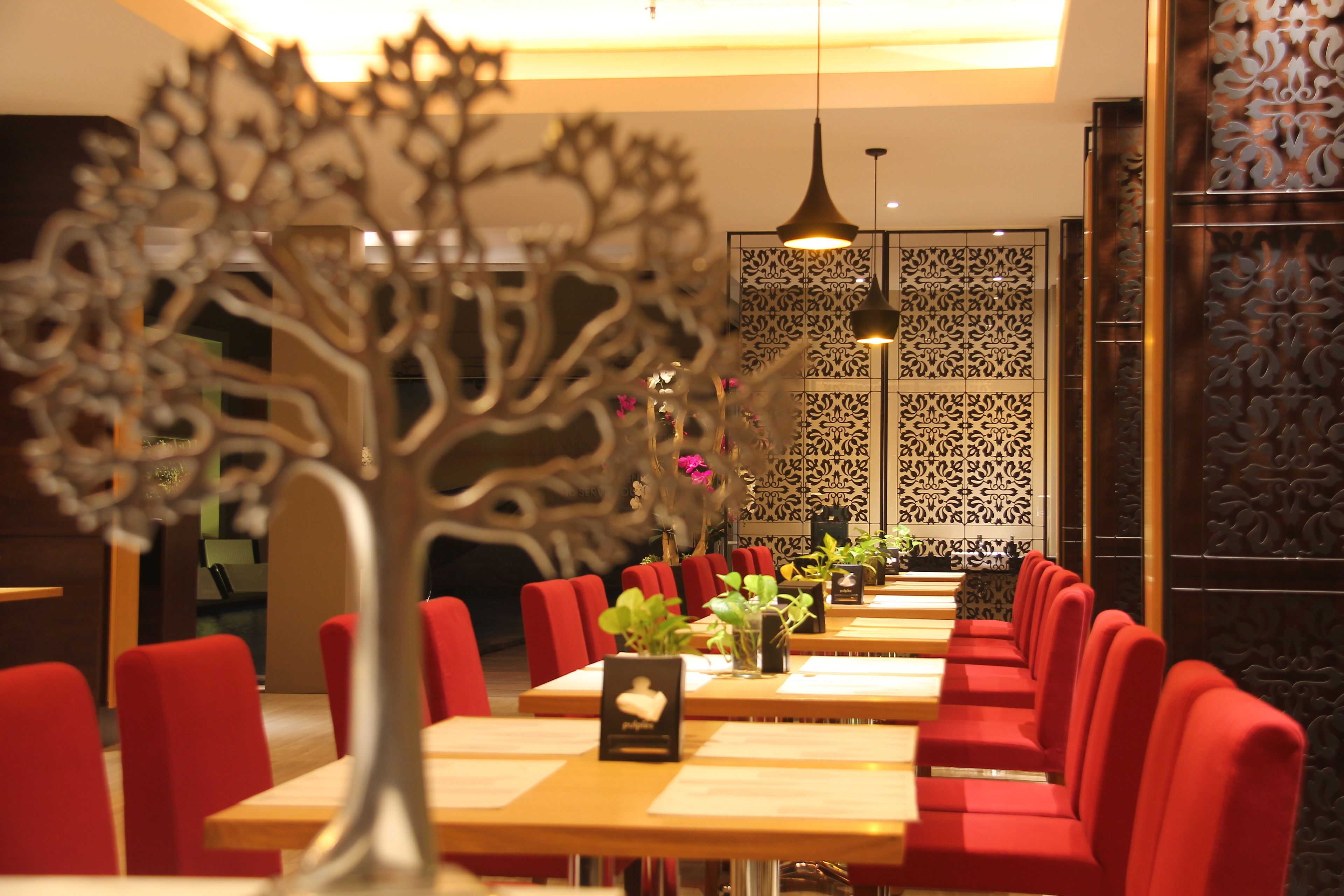 A restaurant with red upholstered chairs, wooden tables, and decorative wall panels.