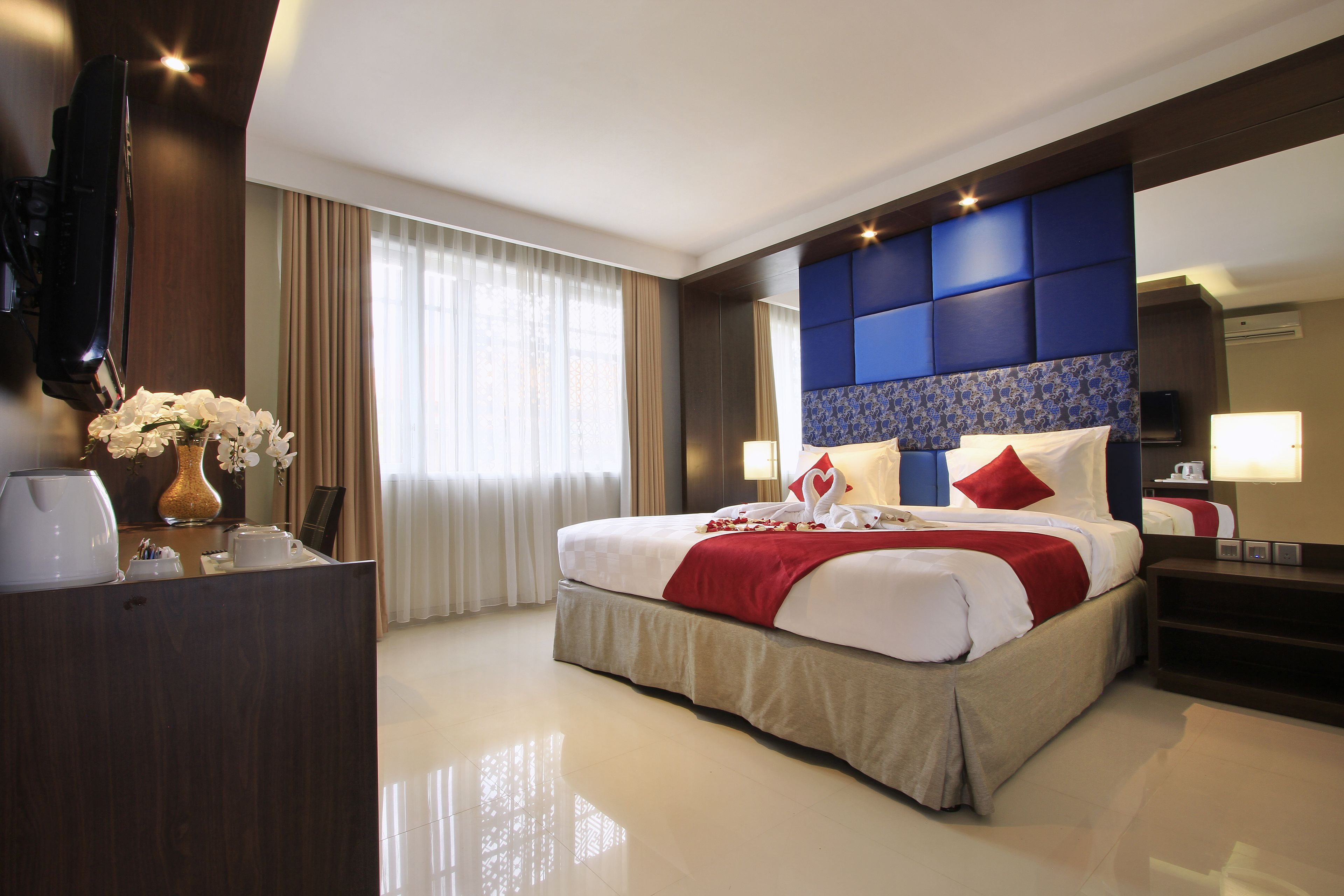 Una habitación de hotel con una cama grande, un escritorio con un jarrón de flores y un televisor.