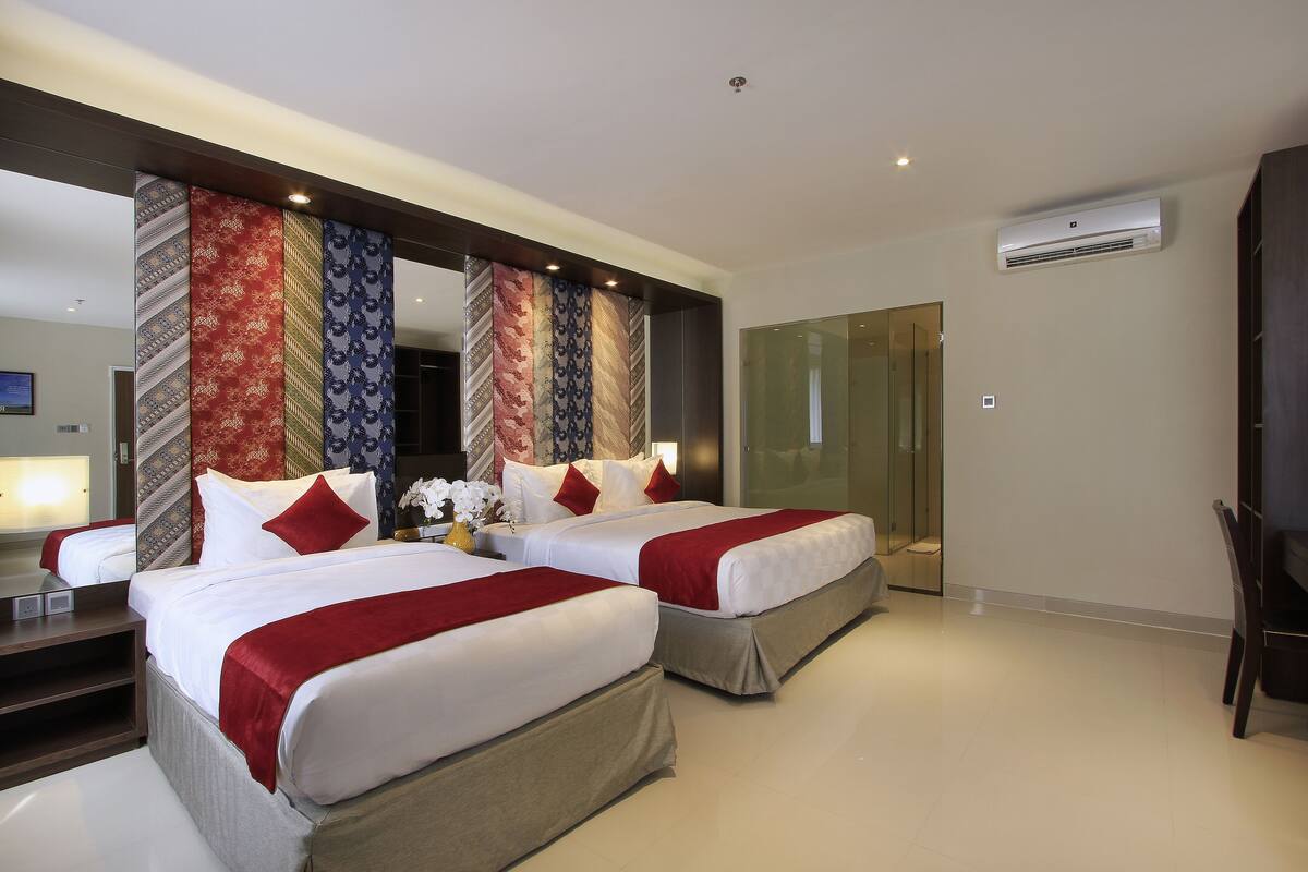 A hotel room with two beds, a large mirror, and an air conditioning unit.