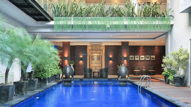 Una piscina con superficie de agua azul cristalina, rodeada de plantas en macetas y muebles modernos.