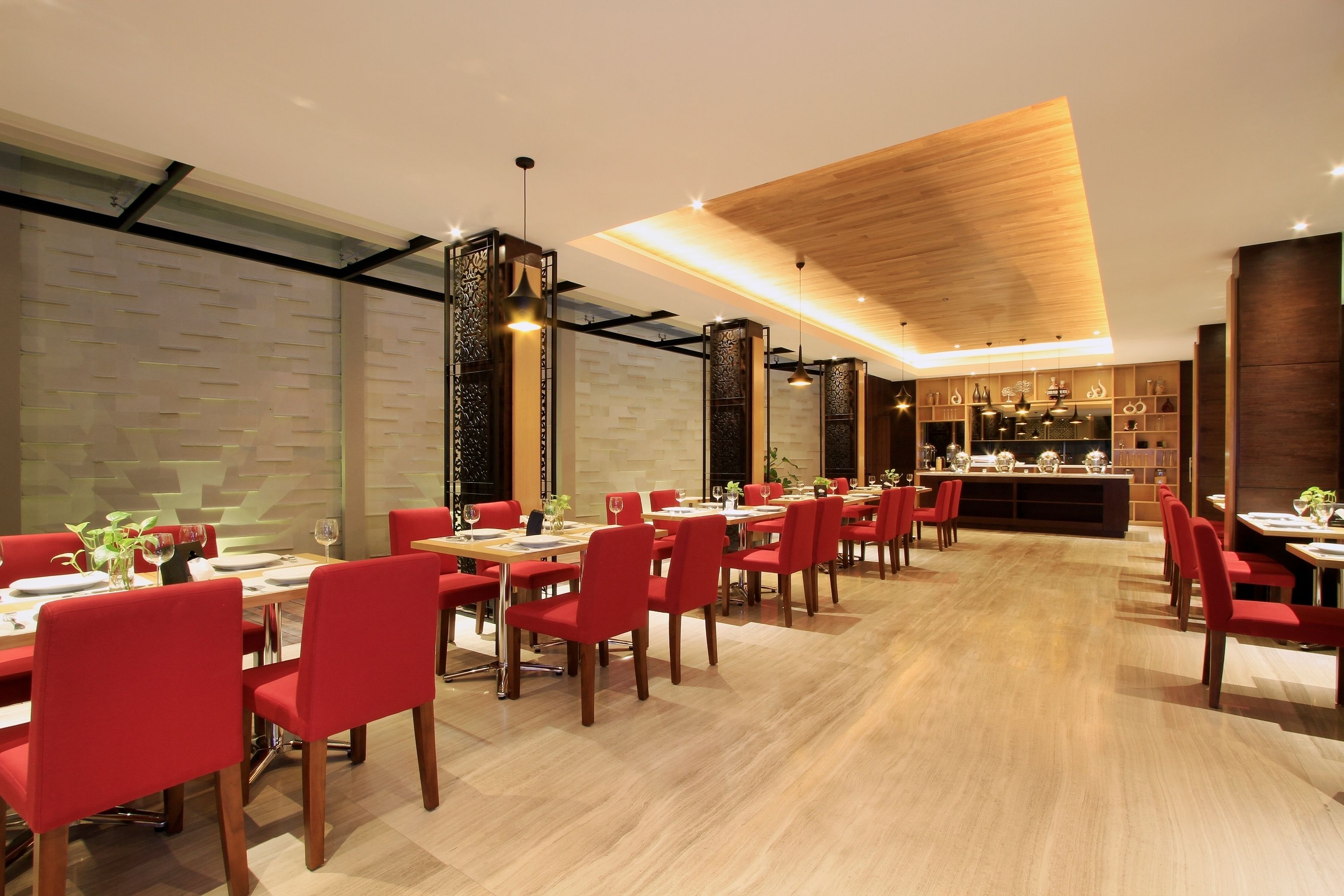 A modern restaurant with red chairs and wooden tables, a bar area, and a patterned wall.