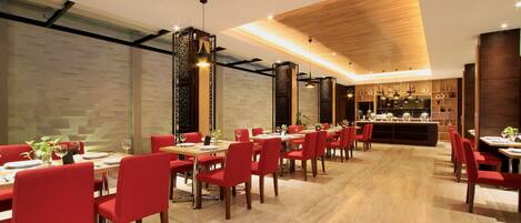A modern restaurant with red chairs and wooden tables, a bar area, and a patterned wall.