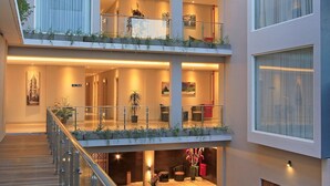 Interior de hotel con varios niveles, balcones, plantas de interior y una terraza de madera.