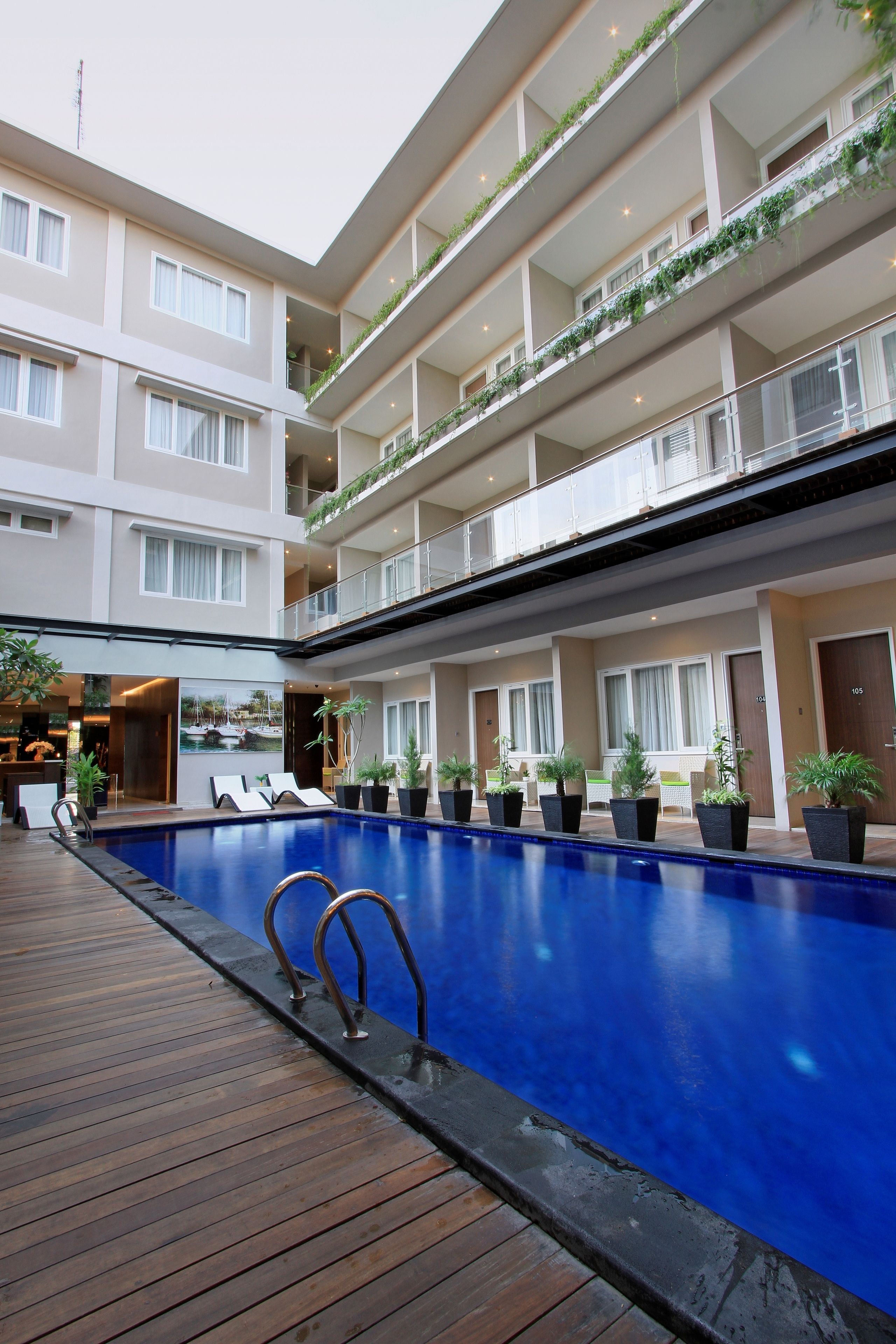Un hotel de varios pisos con piscina central, balcones con plantas y una zona de recepción.