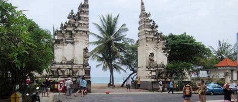 Entrada de un templo con dos torres ornamentales, una palmera y una playa al fondo.