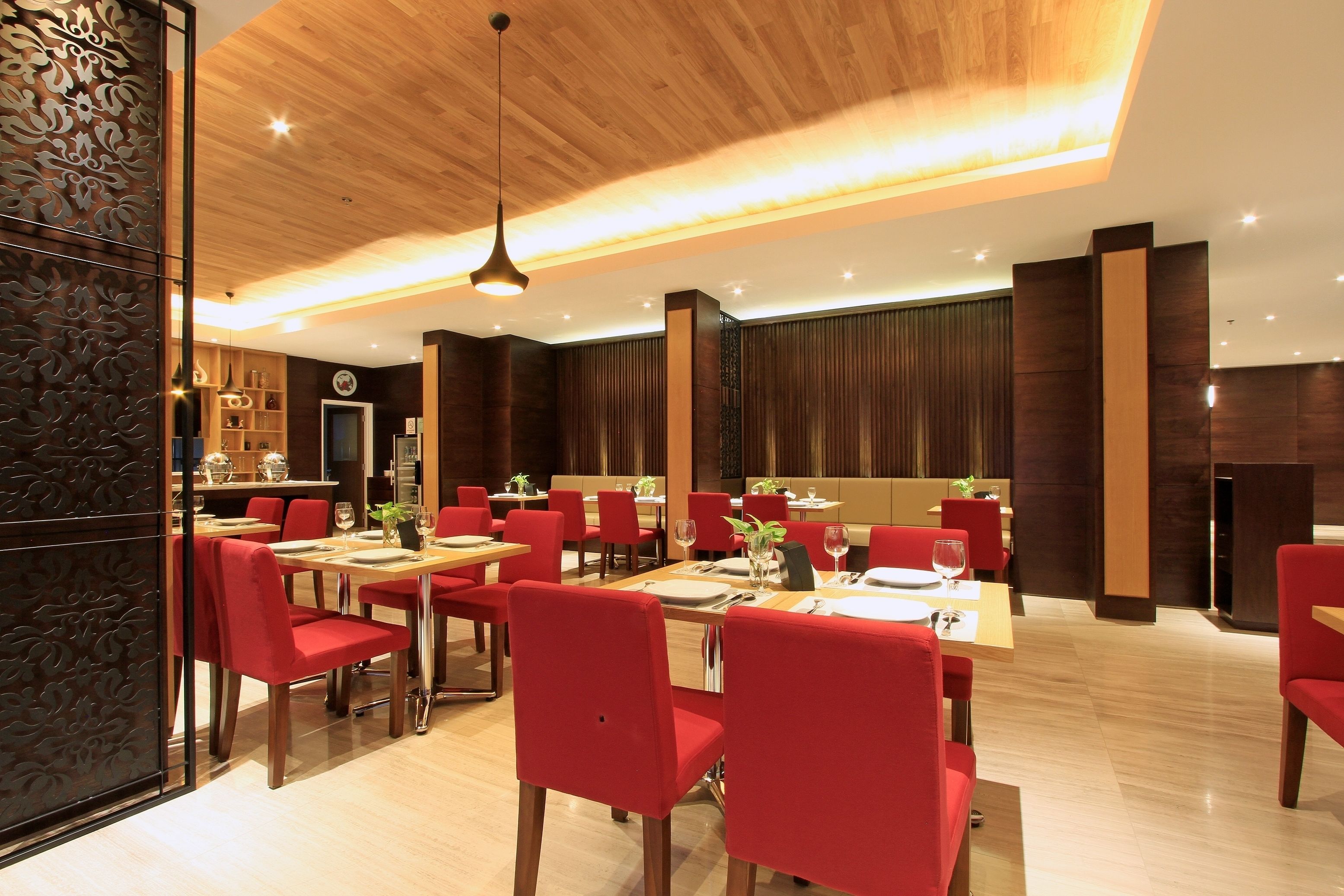 Un comedor moderno con techo de madera, sillas rojas y mesas dispuestas para comer.