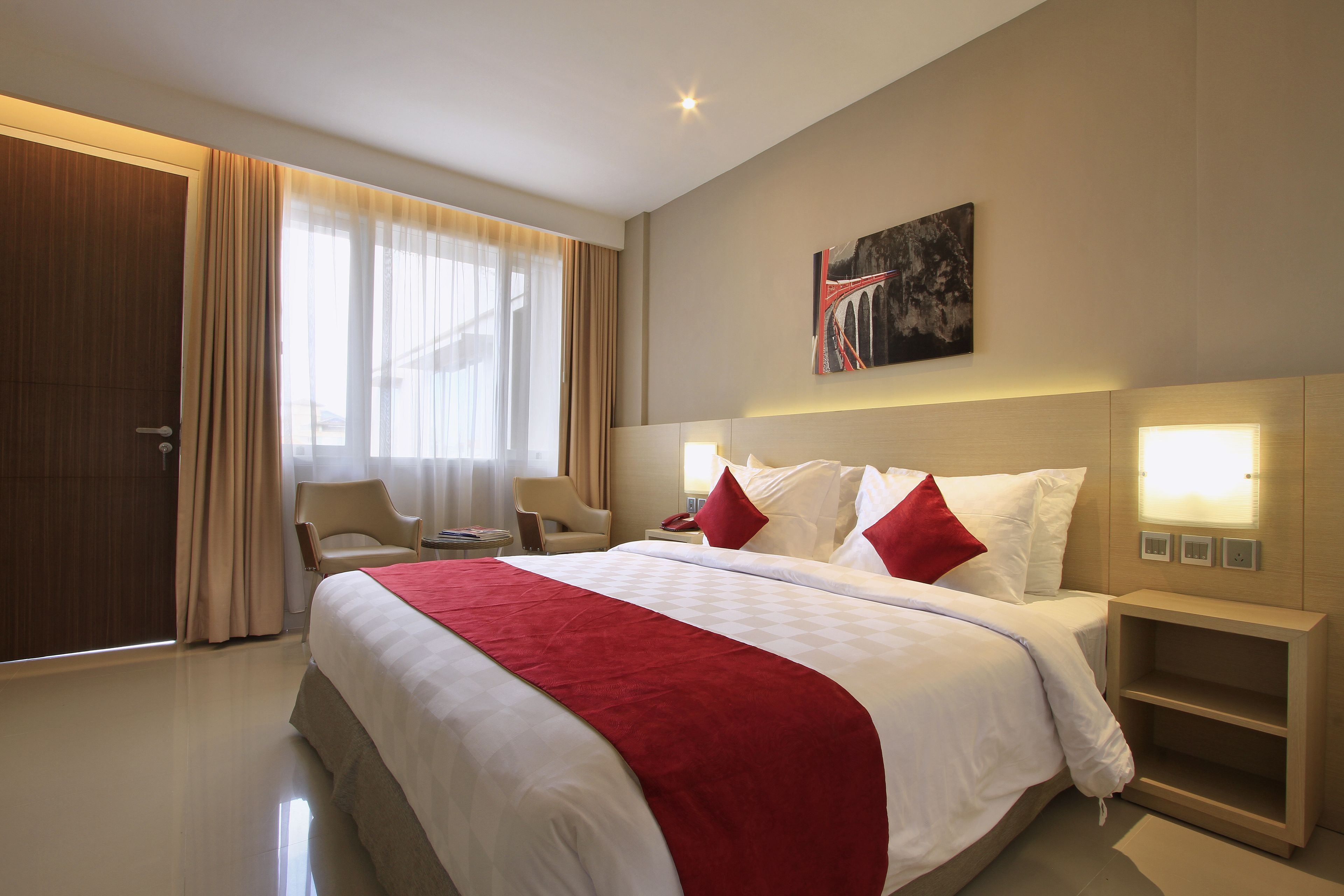 A hotel room with a large bed, a desk, a chair, and a painting on the wall.