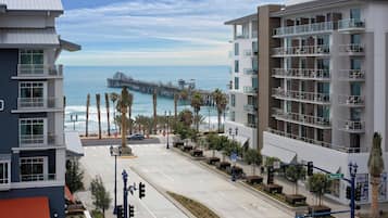 A coastal urban street with modern buildings, a pier, and a clear view of the ocean.