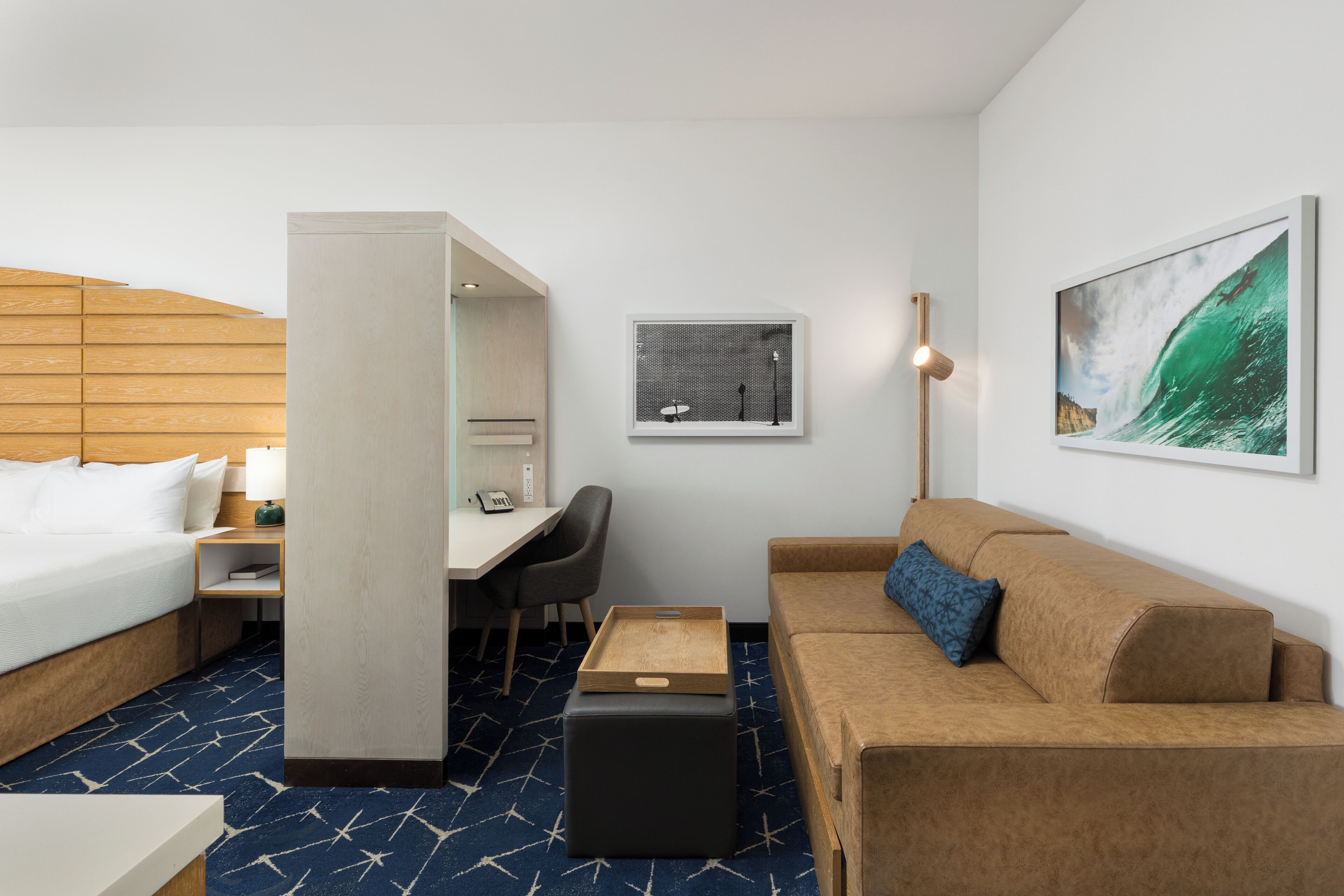 A hotel room with a bed, a desk, a chair, a sofa, a small table, and artwork on the walls.