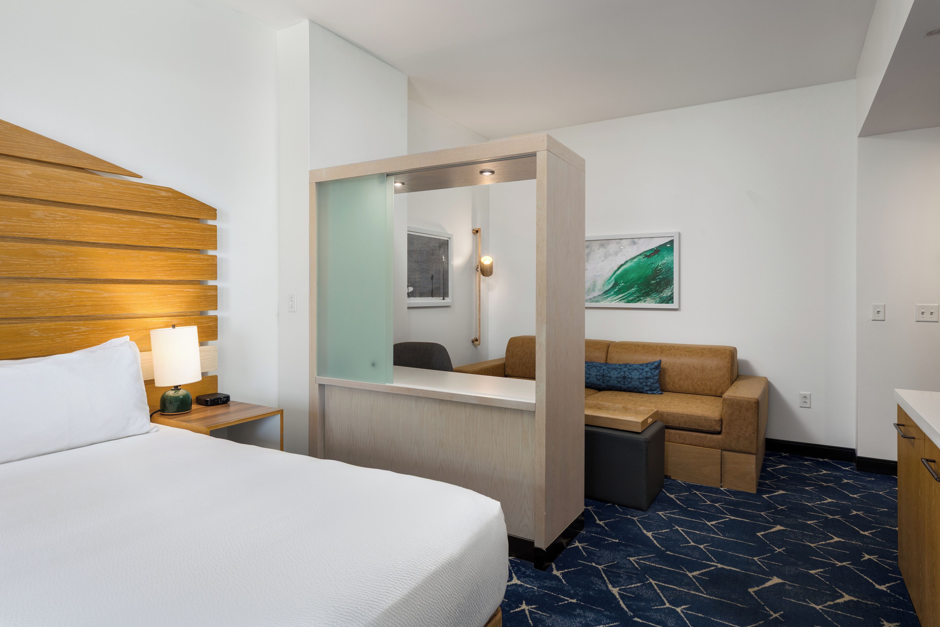 Quarto de hotel com cama grande, escrivaninha com espelho, sofá e mesa pequena.