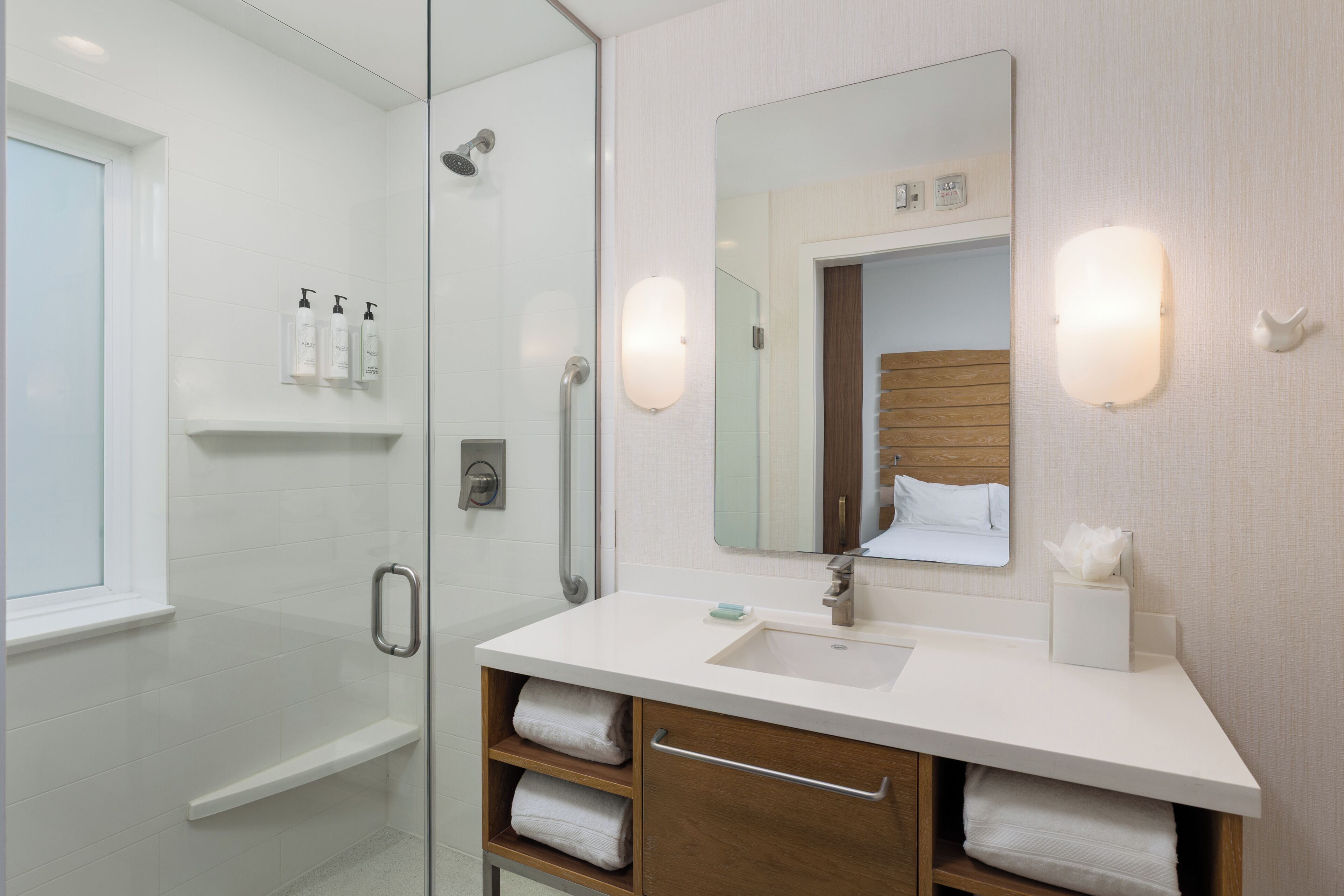 Une salle de bain moderne avec une douche à l’italienne en verre, un lavabo blanc avec un meuble-vasque en bois et un grand miroir.