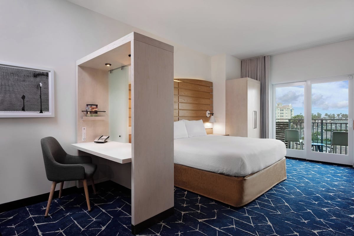 Ein Hotelzimmer mit Bett, Schreibtisch, Stuhl, Kleiderschrank, Fenster mit Aussicht und einem gemusterten Teppich.
