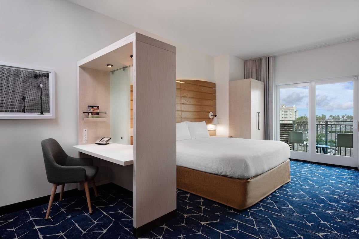 A hotel room with a bed, a desk, a chair, a wardrobe, a window with a view, and a patterned carpet.