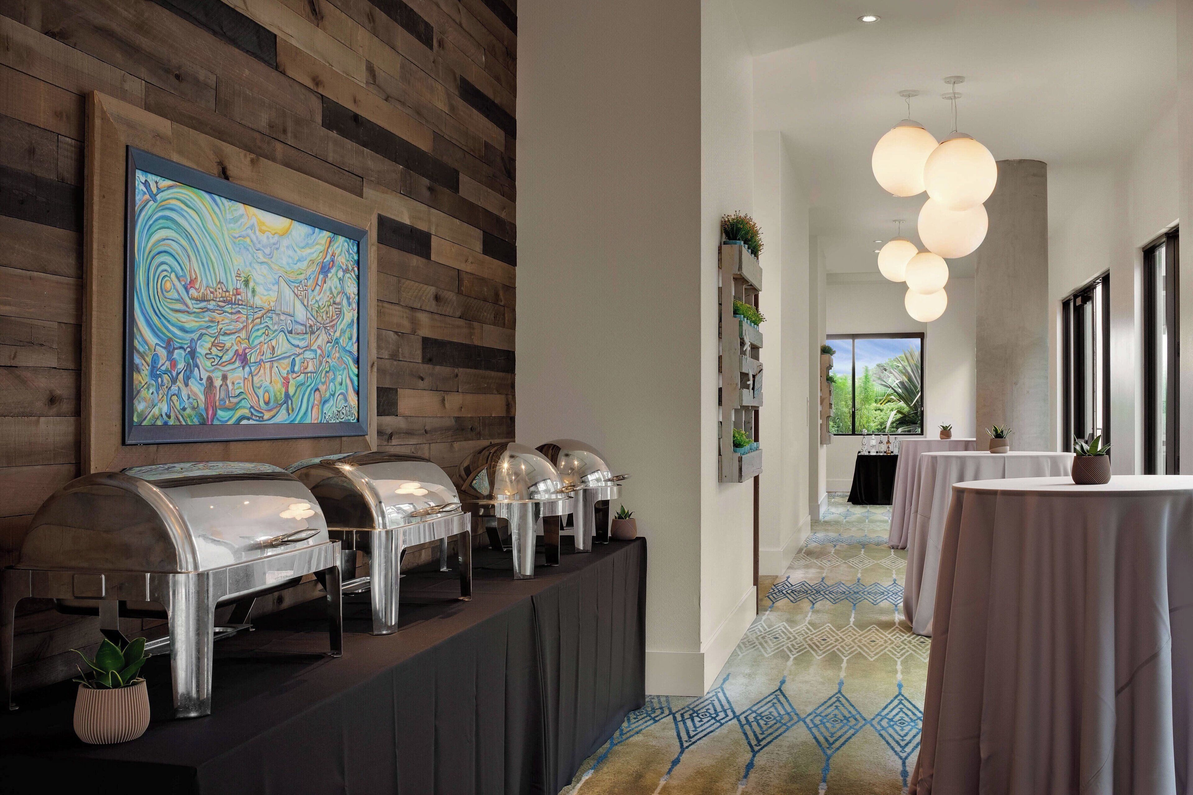 Un buffet avec plusieurs points de service pour la nourriture, un grand tableau abstrait accroché au mur et une moquette à motifs.