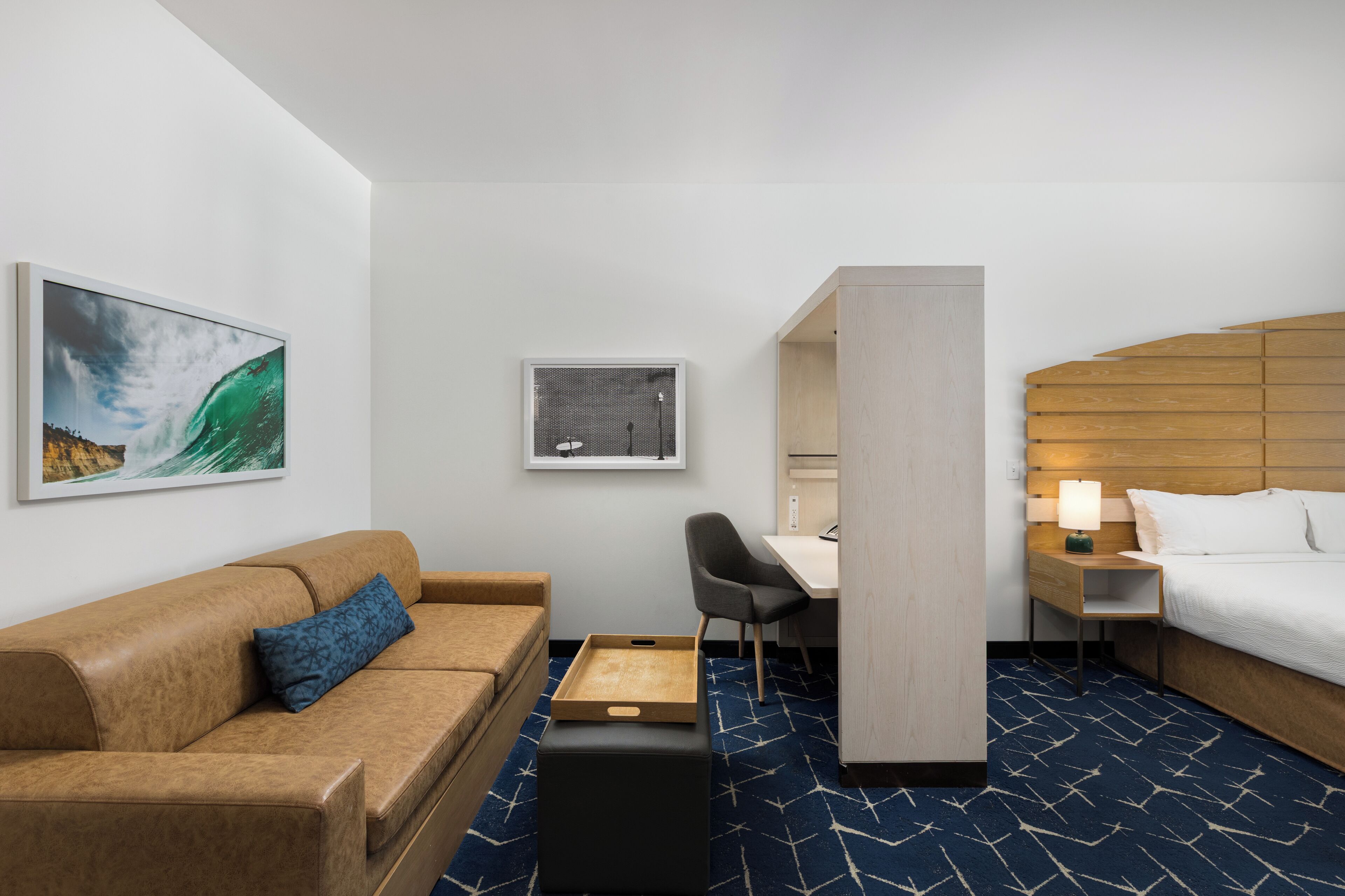 Une chambre d’hôtel comprenant un lit, un bureau, une chaise, un canapé et des œuvres d’art accrochées aux murs.