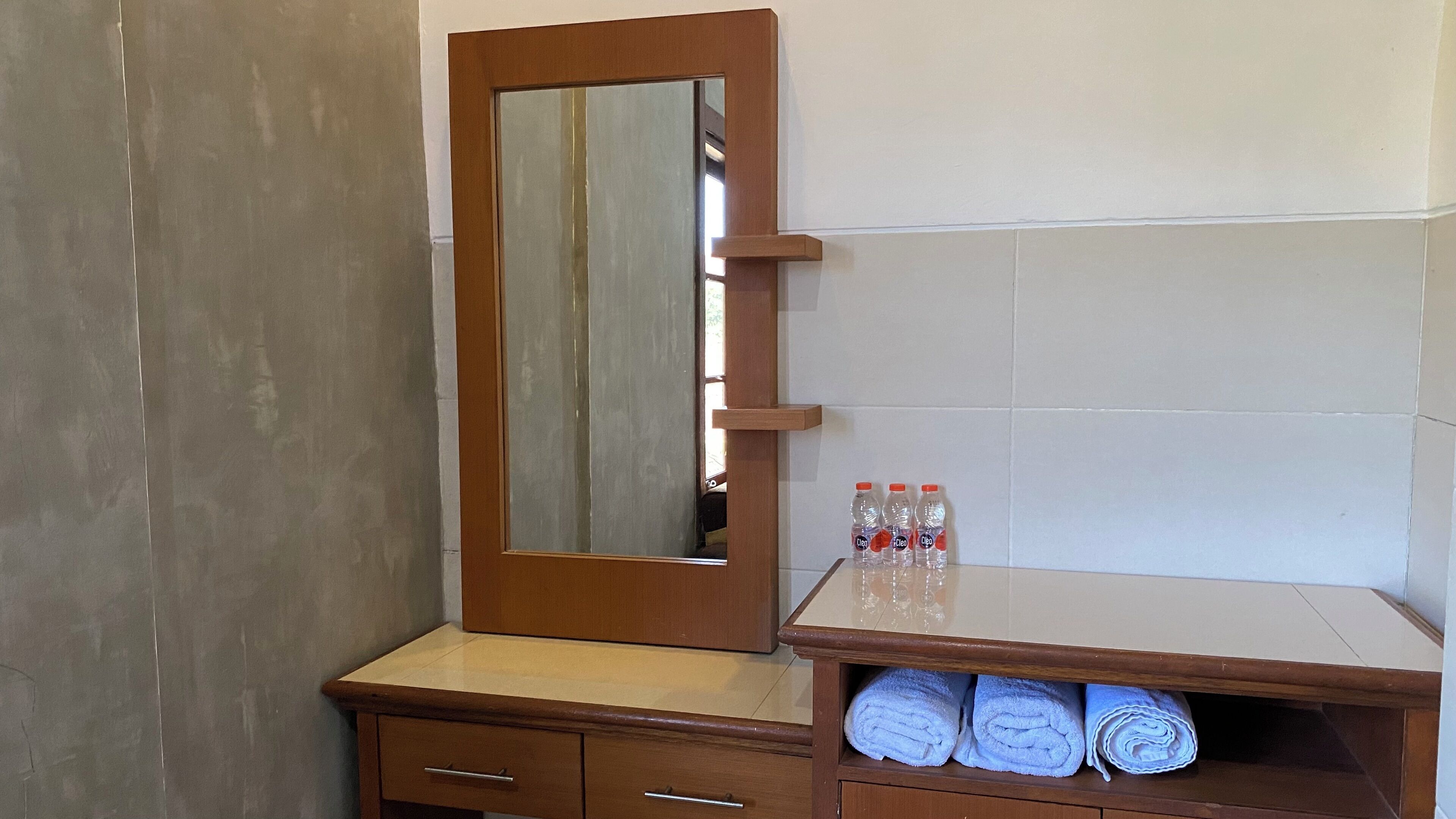 A bathroom vanity with a mirror, a shelf with towels, and a bottle of water.