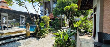 A pool area with stone steps, surrounded by tropical plants and a statue.