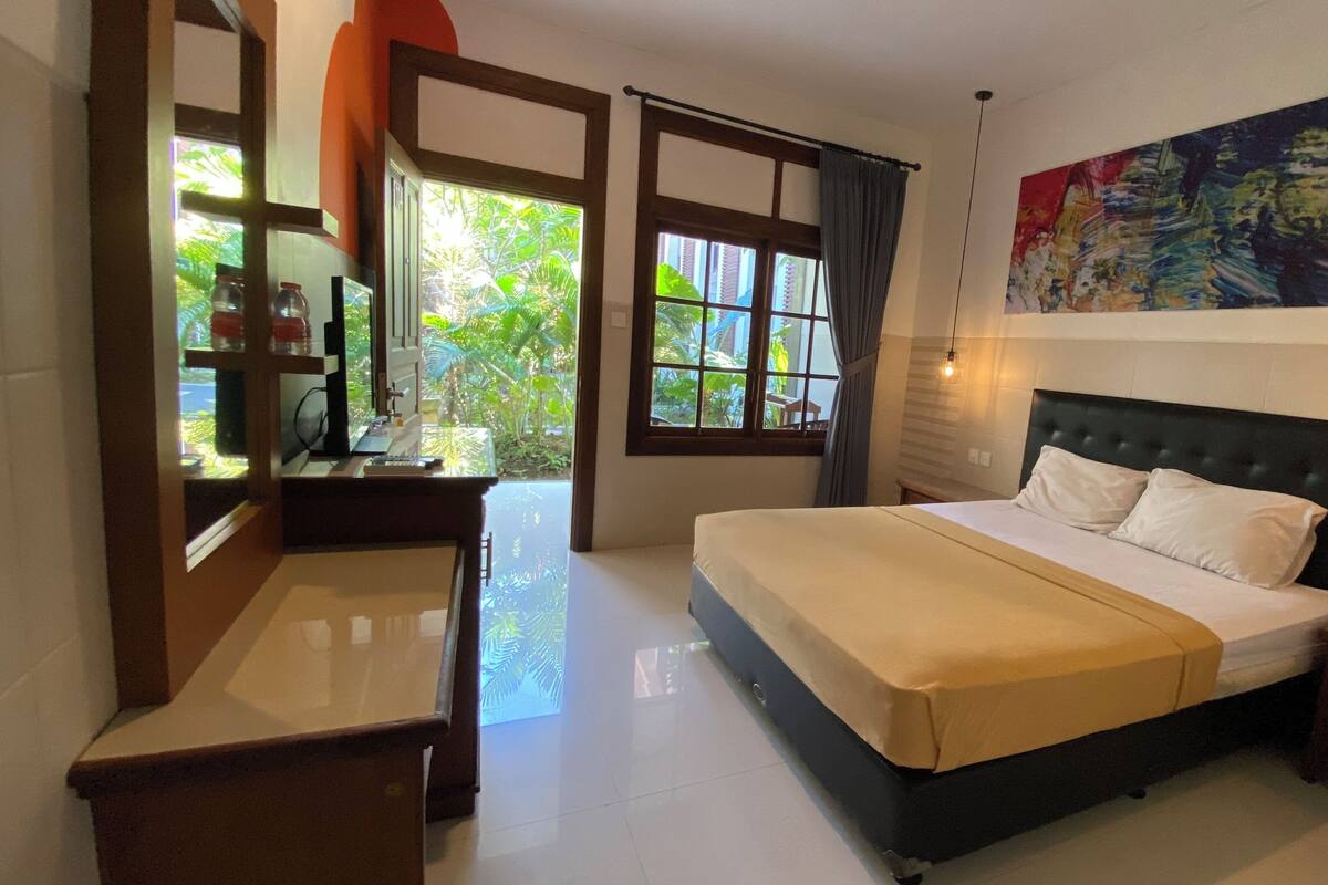 A bedroom with a bed, a desk, a chair, a window with curtains, and a painting on the wall.