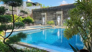 Una piscina con baldosas de piedra, rodeada de follaje y un muro de piedra.