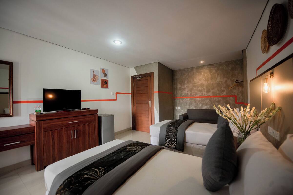A modern hotel room with a bed, a TV, a wooden dresser, and a wall-mounted TV.