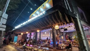 An outdoor restaurant with a thatched roof and multiple dining tables and chairs. - Sandat Hotel Legian (Kuta)