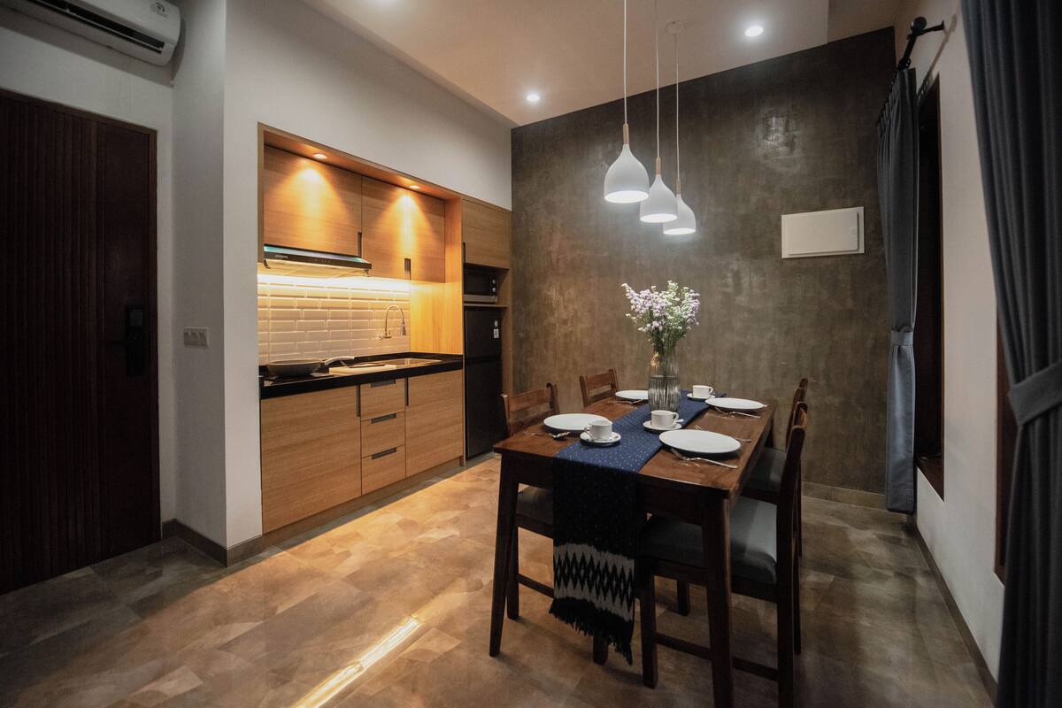 A modern kitchen with wooden cabinets, a dining table set for four, and pendant lights.
