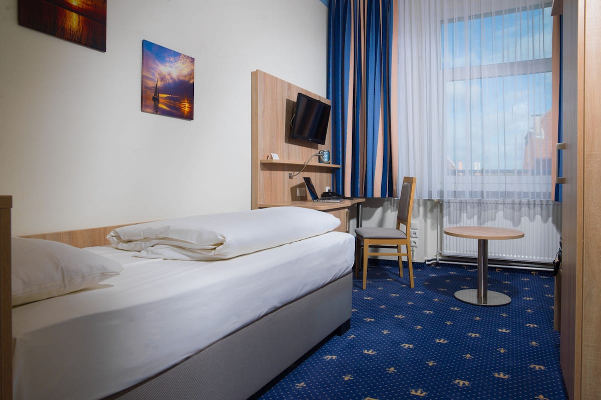 Een hotelkamer met een bed, een bureau, een stoel, een televisie en een raam met gordijnen.