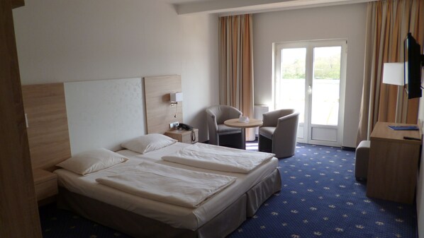 A hotel room with a double bed, a desk, a chair, a small table, and a television. - Hotel Deutscher Kaiser (Lübeck)